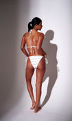 Model wearing white frilly triangle bikini with strappy ties – back view on plain background