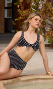 Model in a black and white polka dot bikini sitting by a pool.
