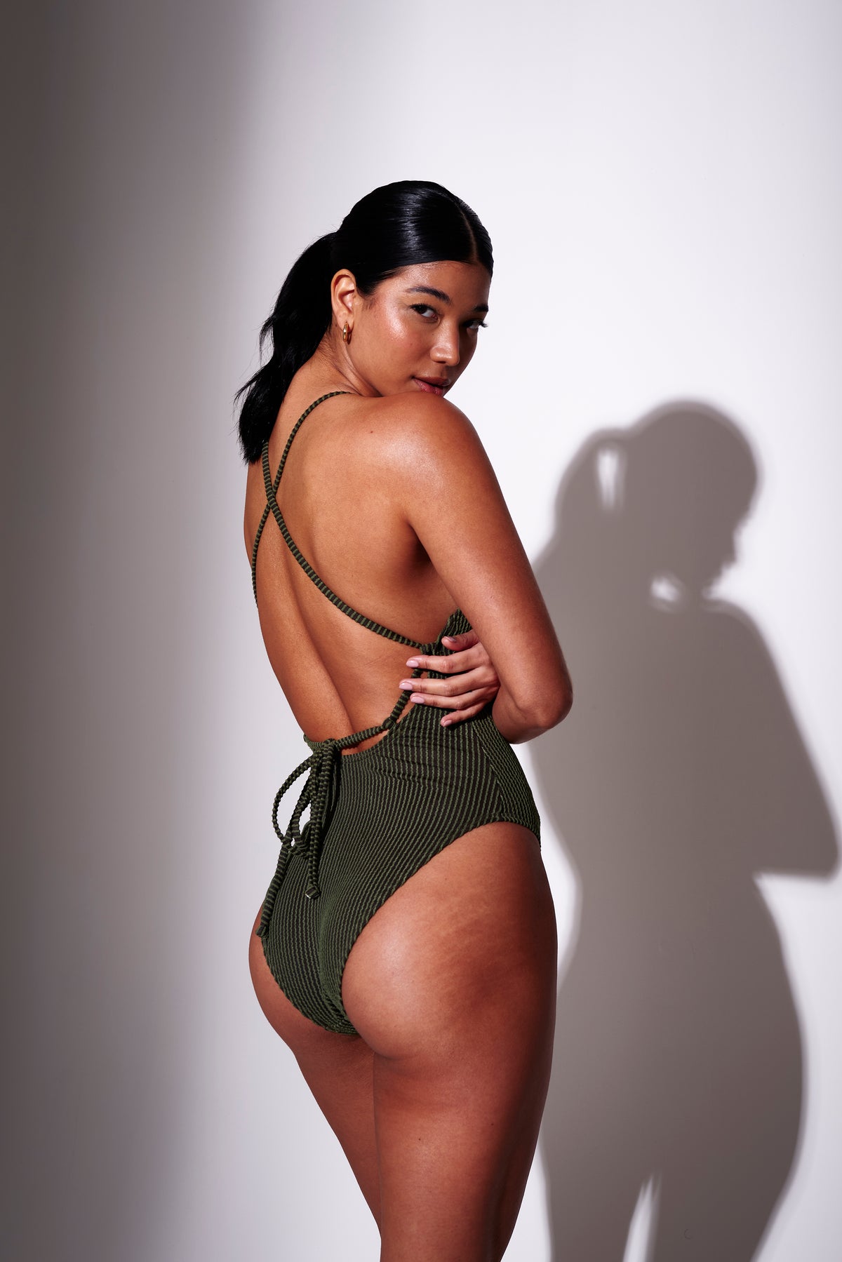 Model wearing a khaki green backless swimsuit against a white background