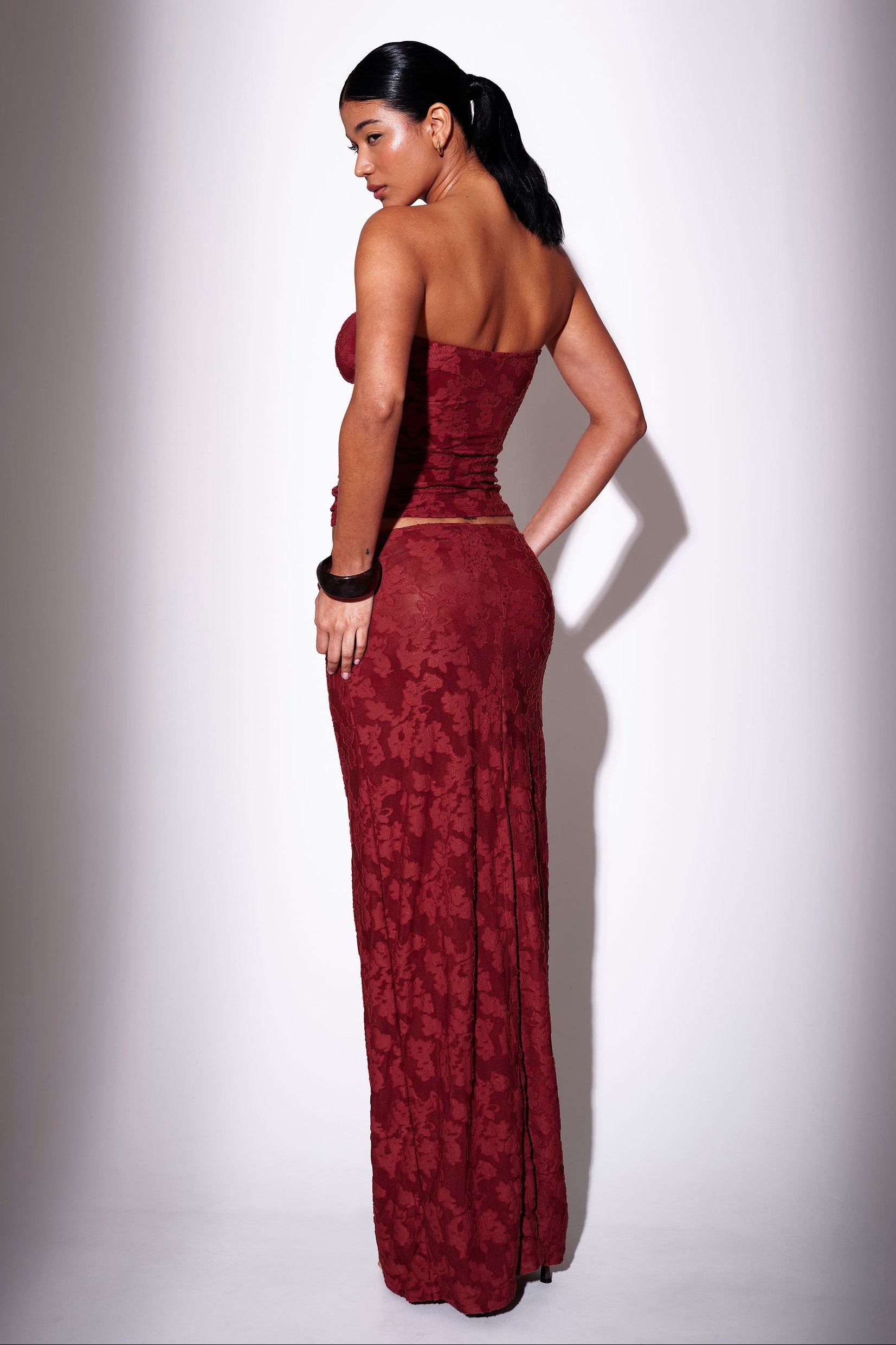 Model wearing a burgundy floral print bandeau top with matching maxi skirt - back view on plain background