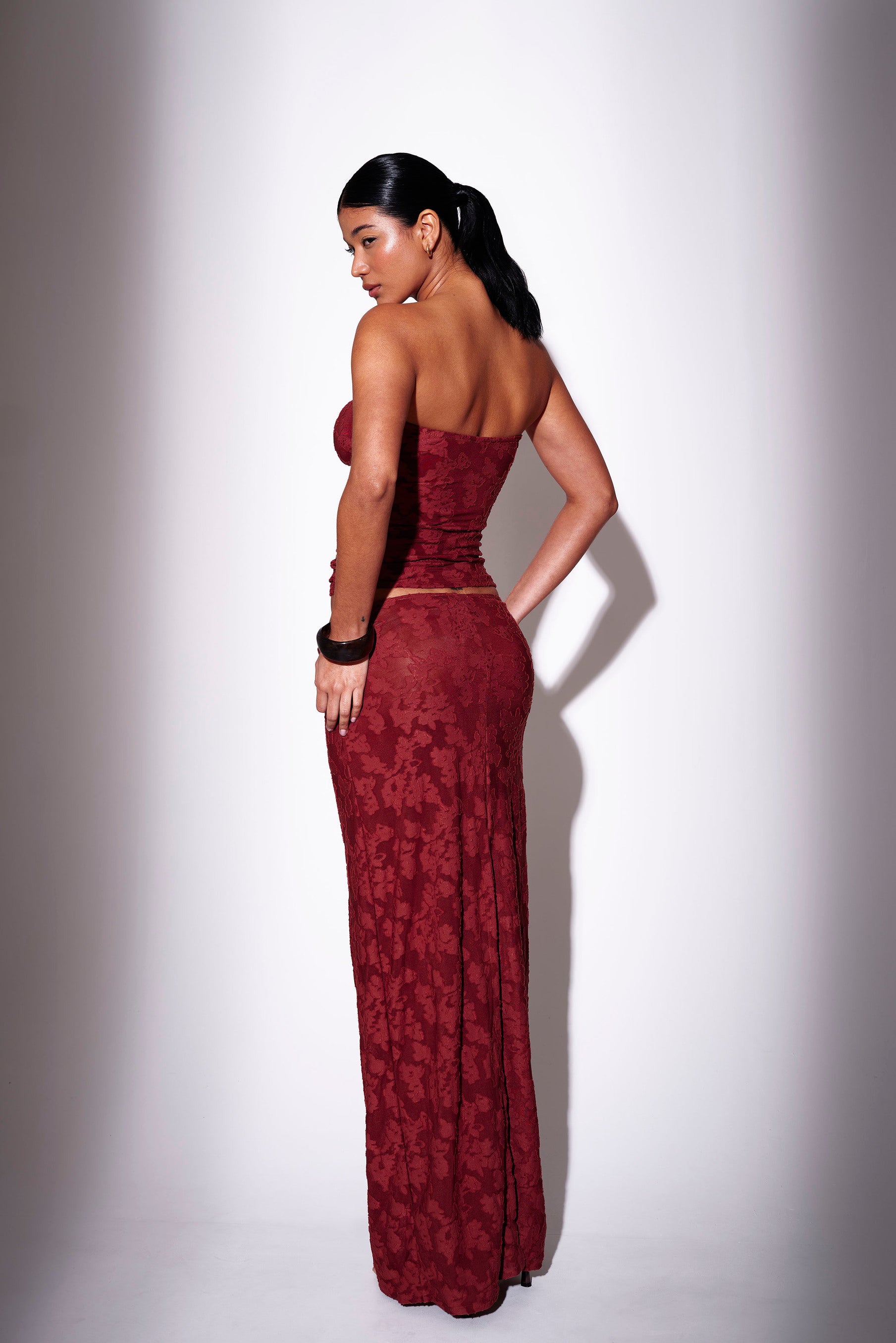 Model wearing a burgundy floral print bandeau top with matching maxi skirt - back view on plain background