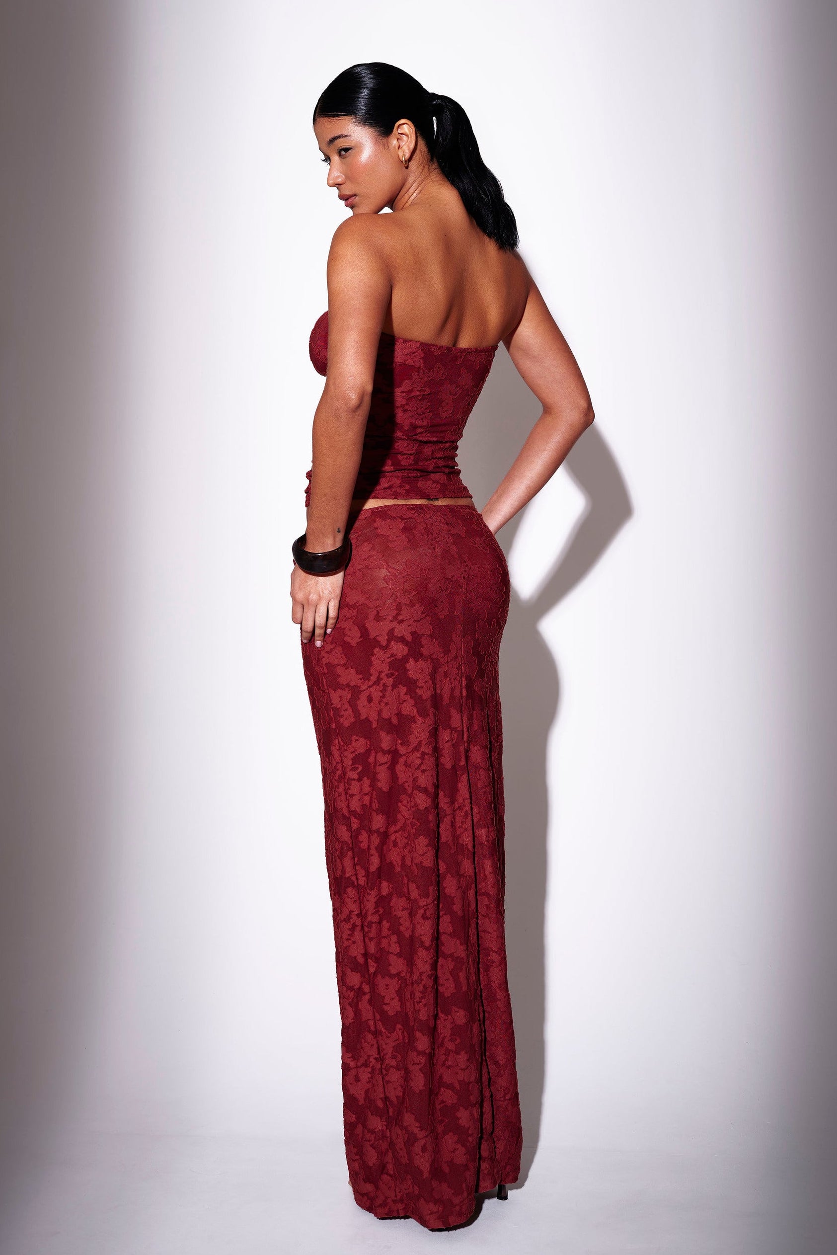 Model wearing a burgundy floral print bandeau top with matching maxi skirt - back view on plain background