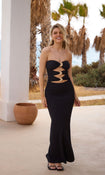 Model in a black strapless dress with cutouts standing outdoors with palm trees in the background