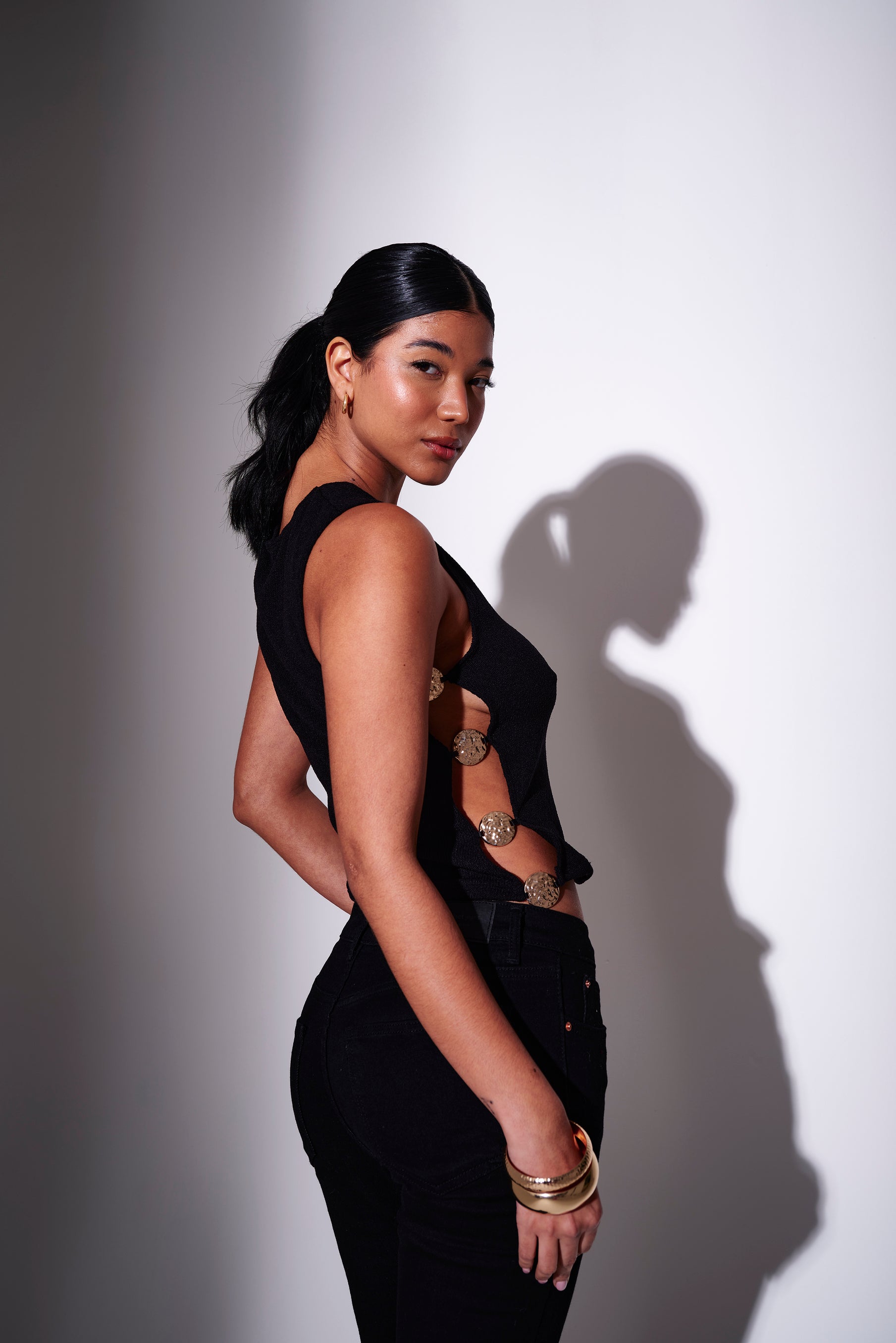 Model in black jeans and a black top with cut-out design - side view on a white background