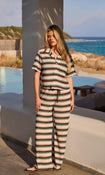 Model in a striped shirt and trouser crochet co-ord standing by a pool with ocean view
