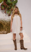 Model in a white linen mini dress and brown cowboy boots standing with cacti in the background