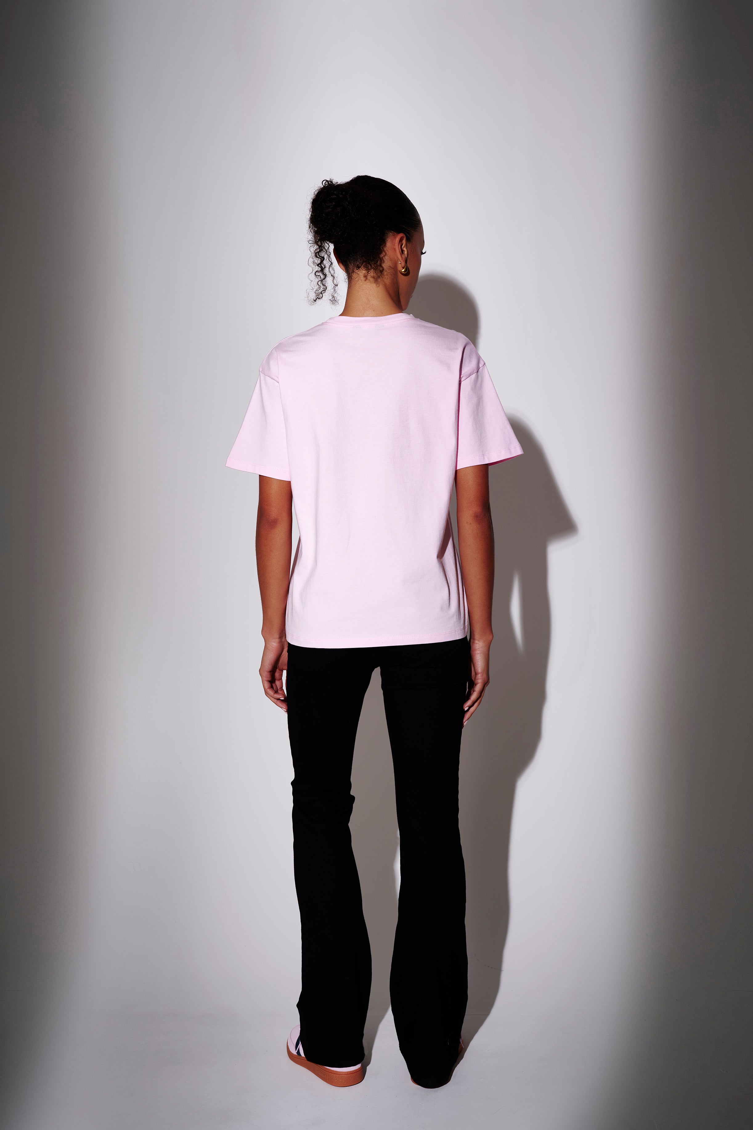 Model wearing a light pink t-shirt and black pants - back view on plain background