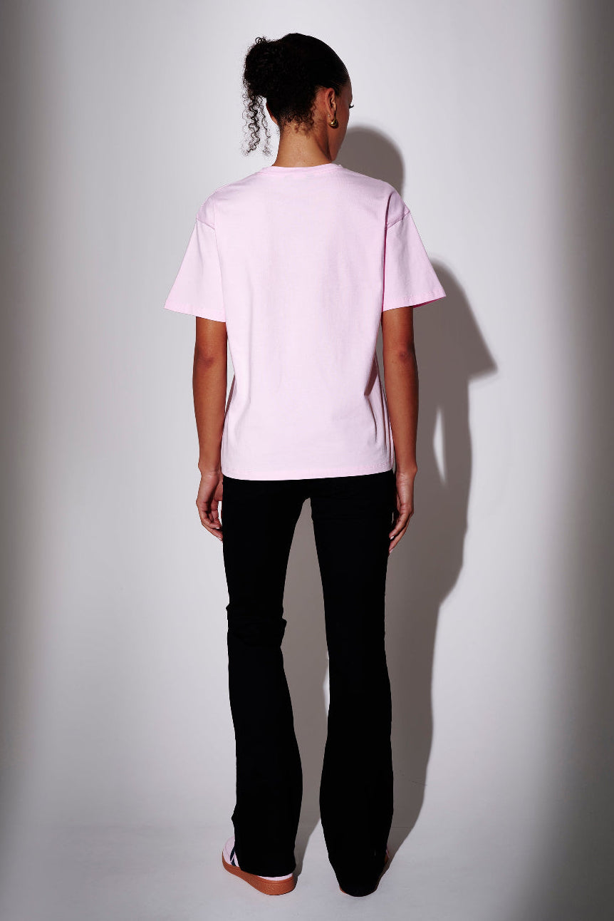 Model wearing a light pink t-shirt and black pants - back view on plain background
