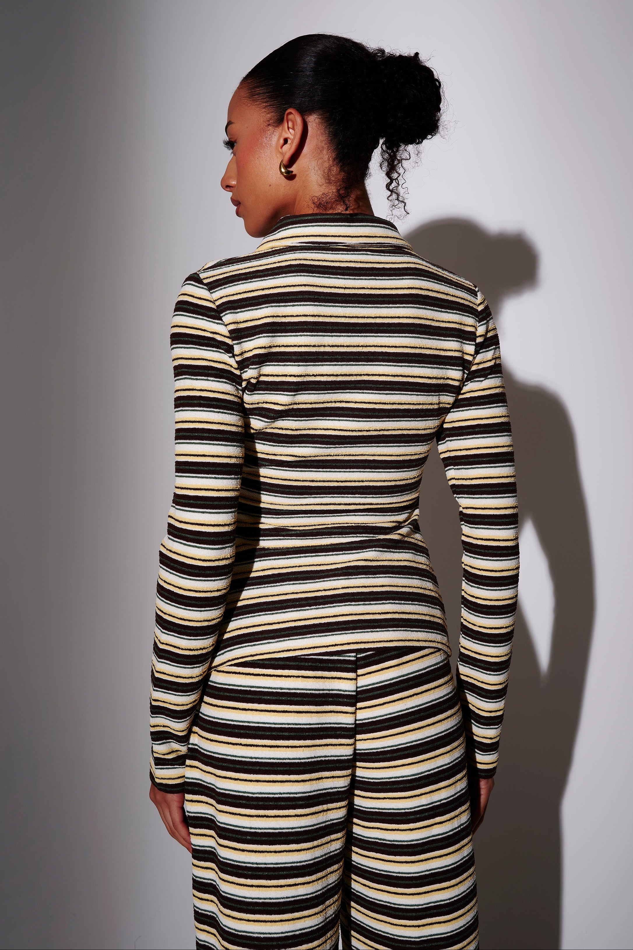 Model wearing a towelling fabric black and yellow striped long sleeve top- back view on plain background